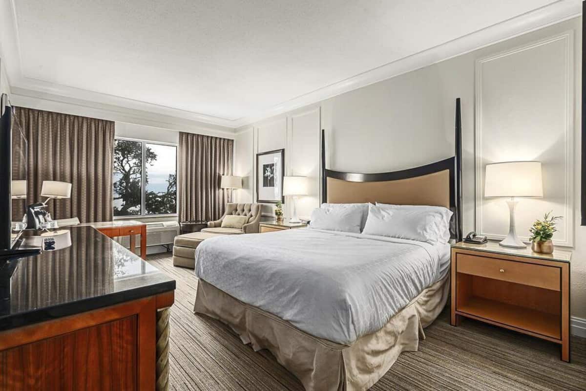A hotel room with a bed, a desk, a chair, a nightstand, and a window with curtains.