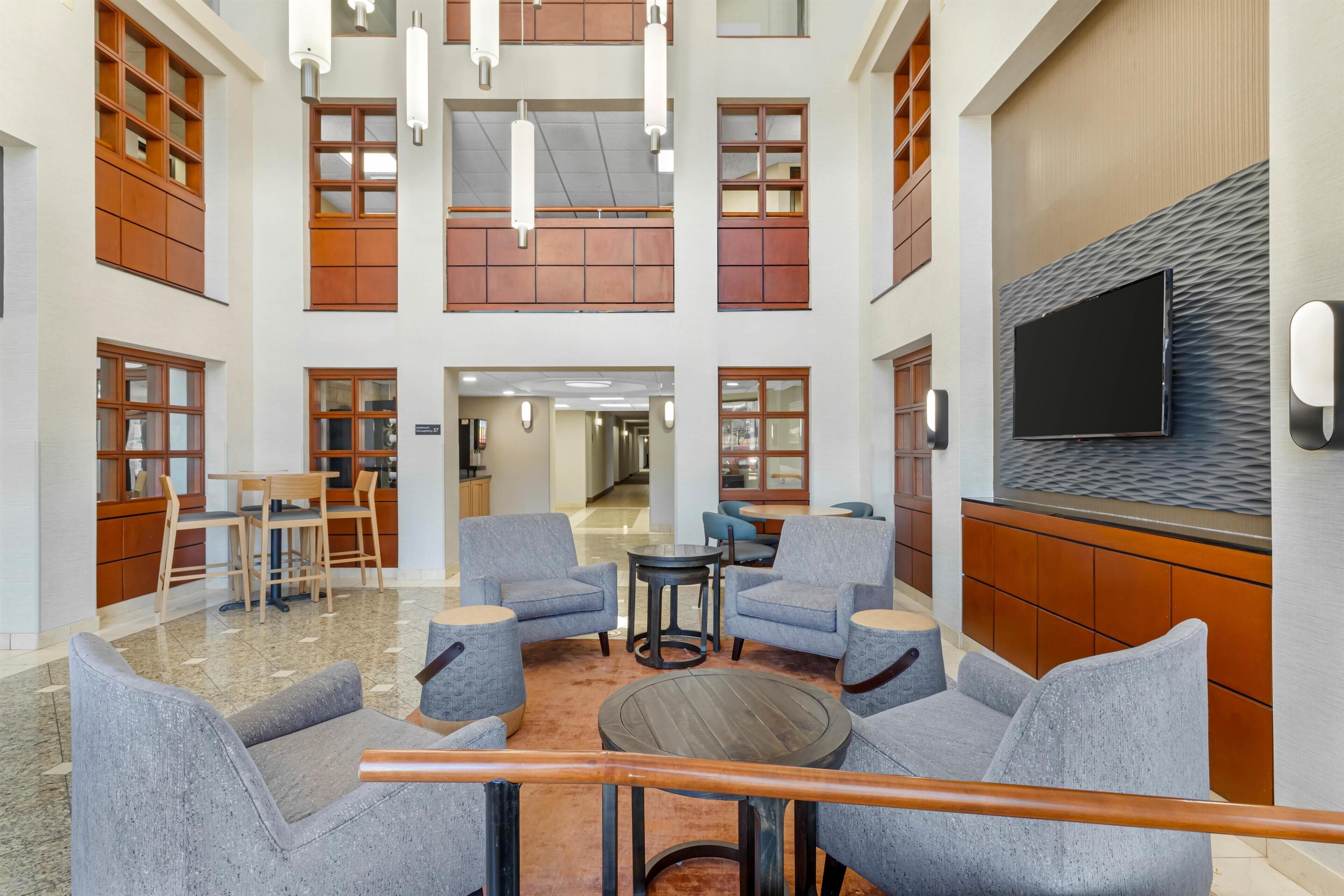 A spacious lobby with multiple seating areas, a flat-screen TV mounted on a textured wall, and a wooden reception desk.