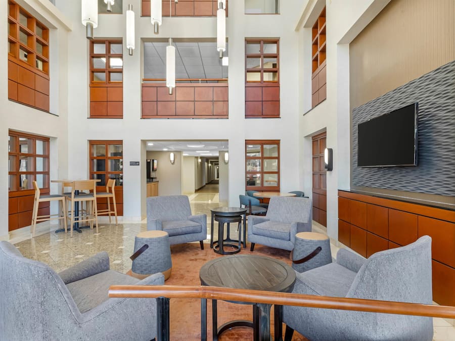 A spacious lobby with multiple seating areas, a flat-screen TV mounted on a textured wall, and a wooden reception desk.