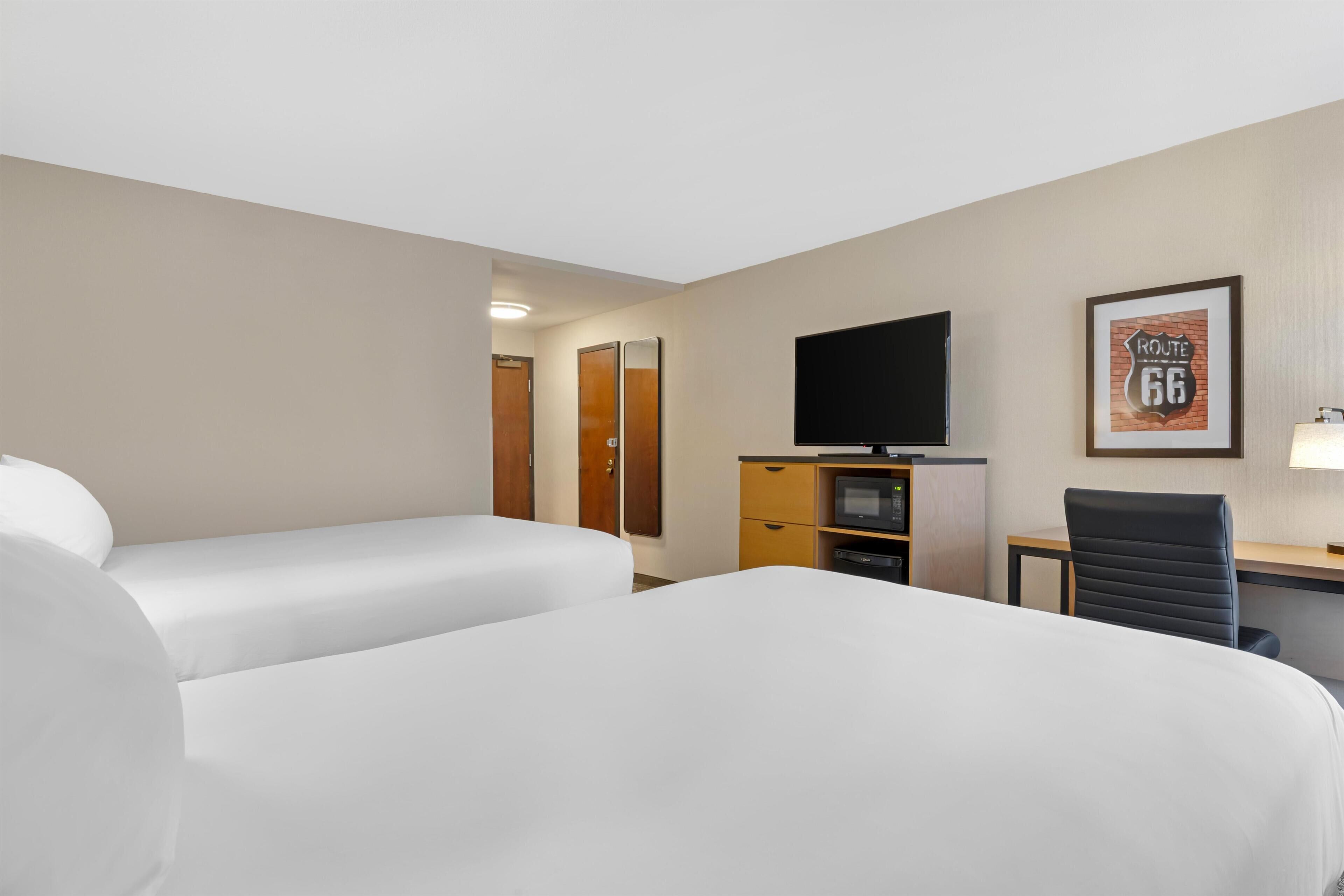 A hotel room with two beds, a desk, a television, a framed picture, and a door leading to another room.