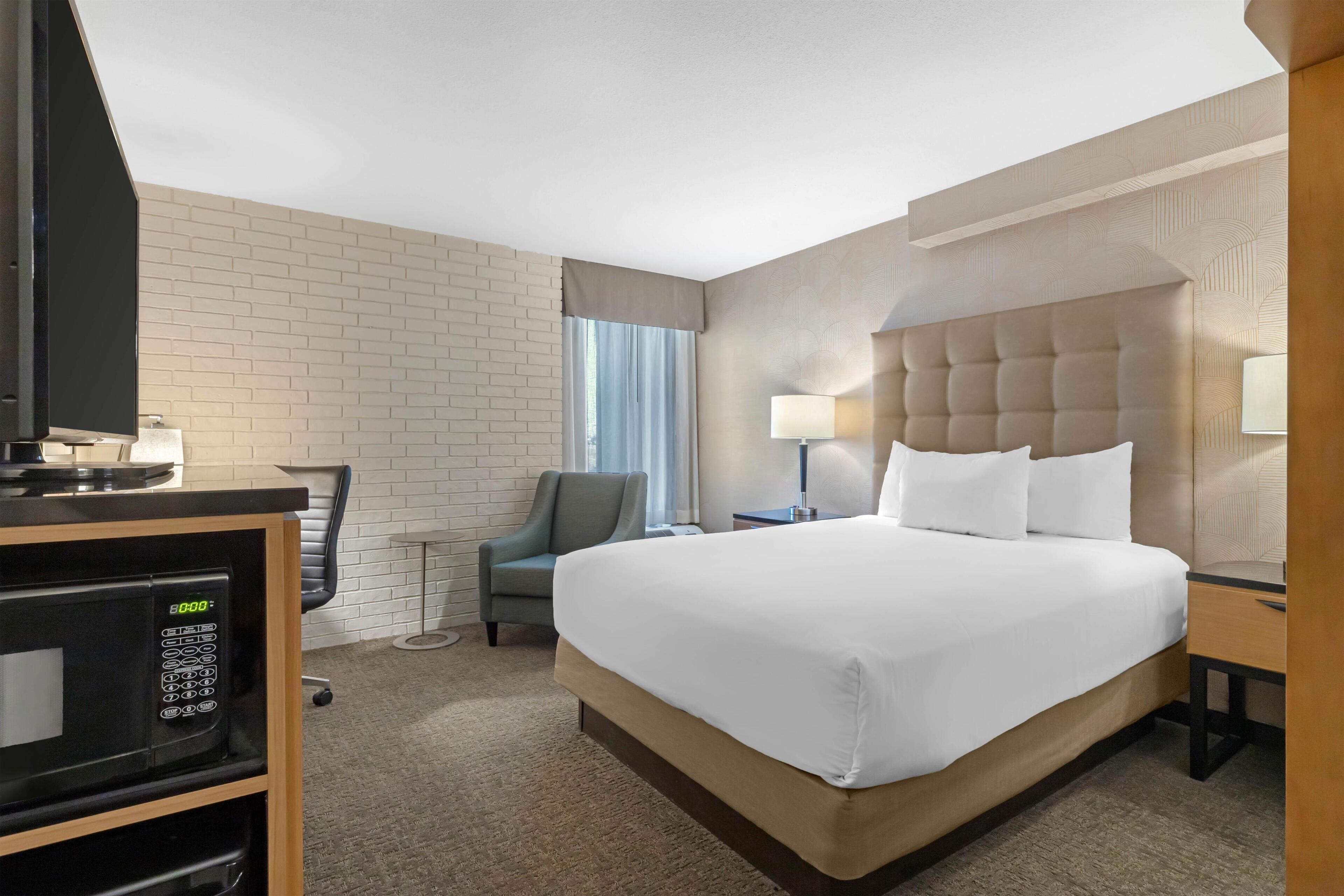 Una habitación de hotel con cama, televisión, silla, escritorio y microondas.