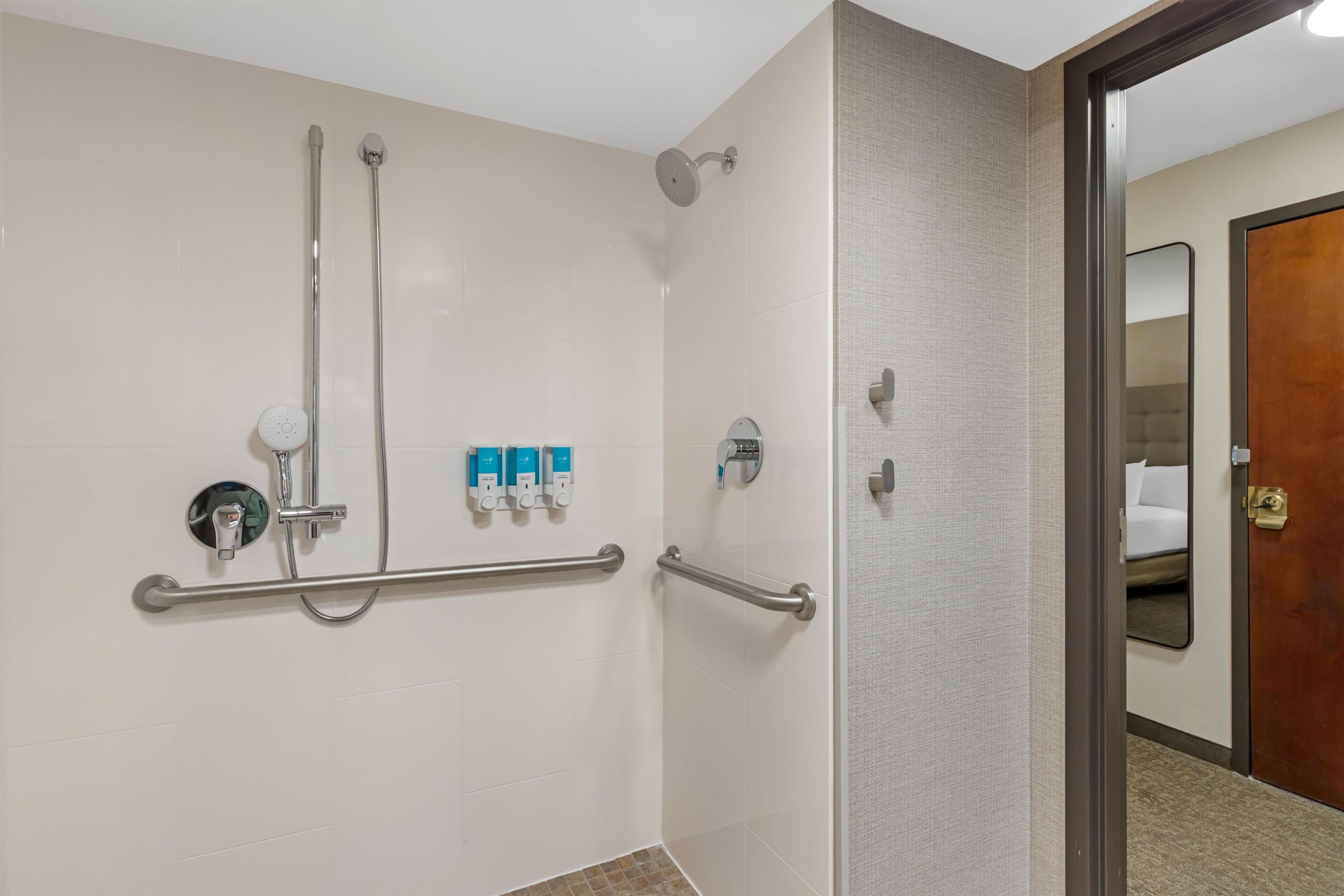 A shower area with grab bars, a handheld showerhead, and a wall-mounted control panel.