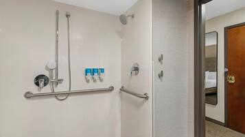 A shower area with grab bars, a handheld showerhead, and a wall-mounted control panel.