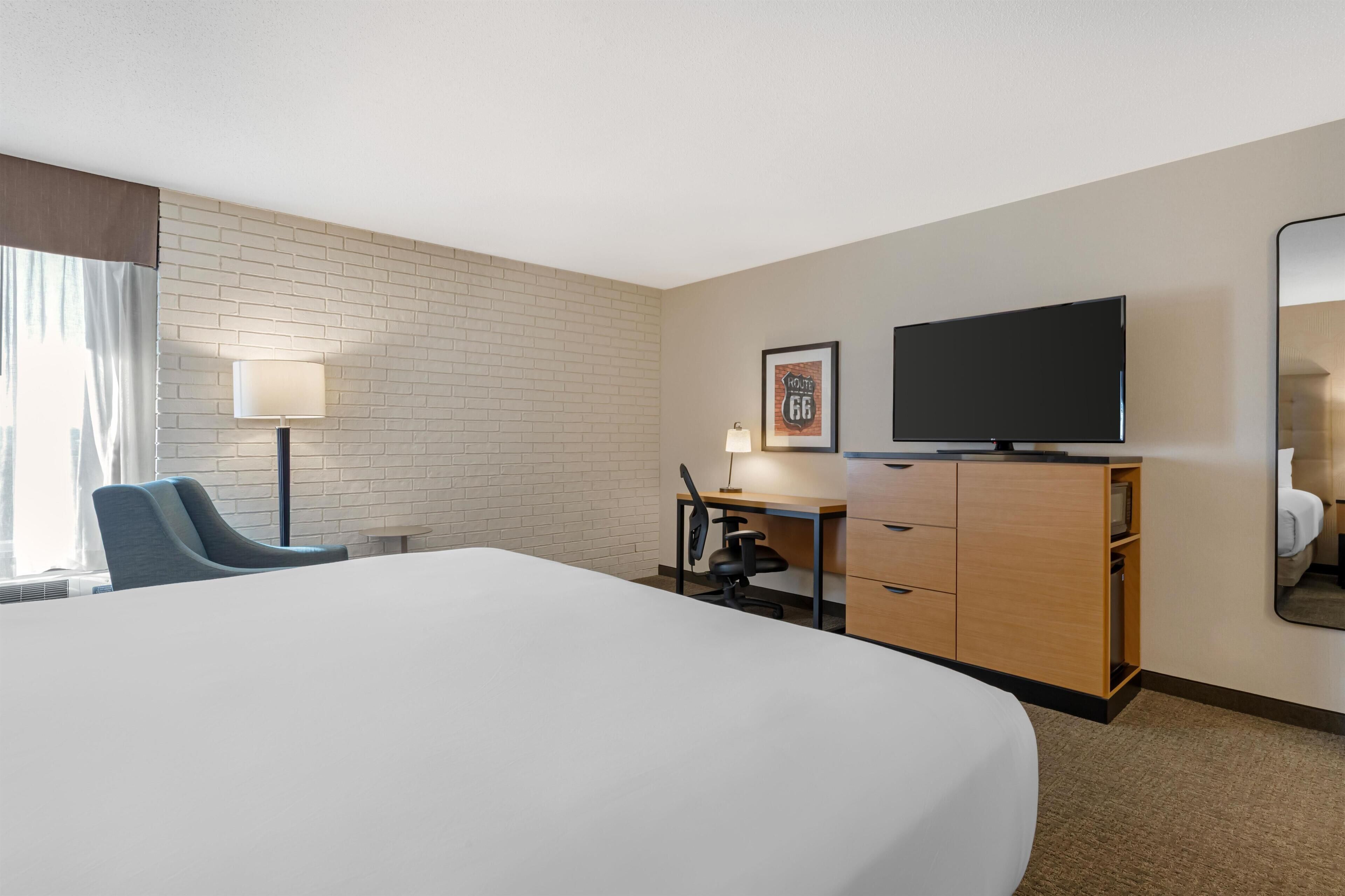 A hotel room with a large bed, a desk with a chair, a television, a mirror, and a wall with a brick pattern.