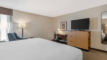 A hotel room with a large bed, a desk with a chair, a television, a mirror, and a wall with a brick pattern.