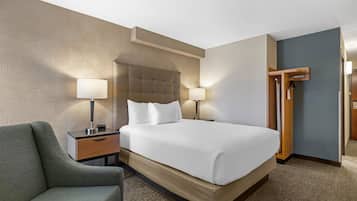 A hotel room with a large bed, two bedside tables with lamps, a chair, a wardrobe, and a patterned wall.