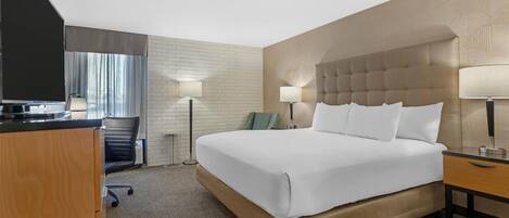 A hotel room with a large bed, a desk, a chair, and a television.