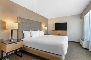 Una habitación de hotel con una cama grande, dos mesitas de noche con lámparas, un televisor de pantalla plana y un equipo de aire acondicionado.
