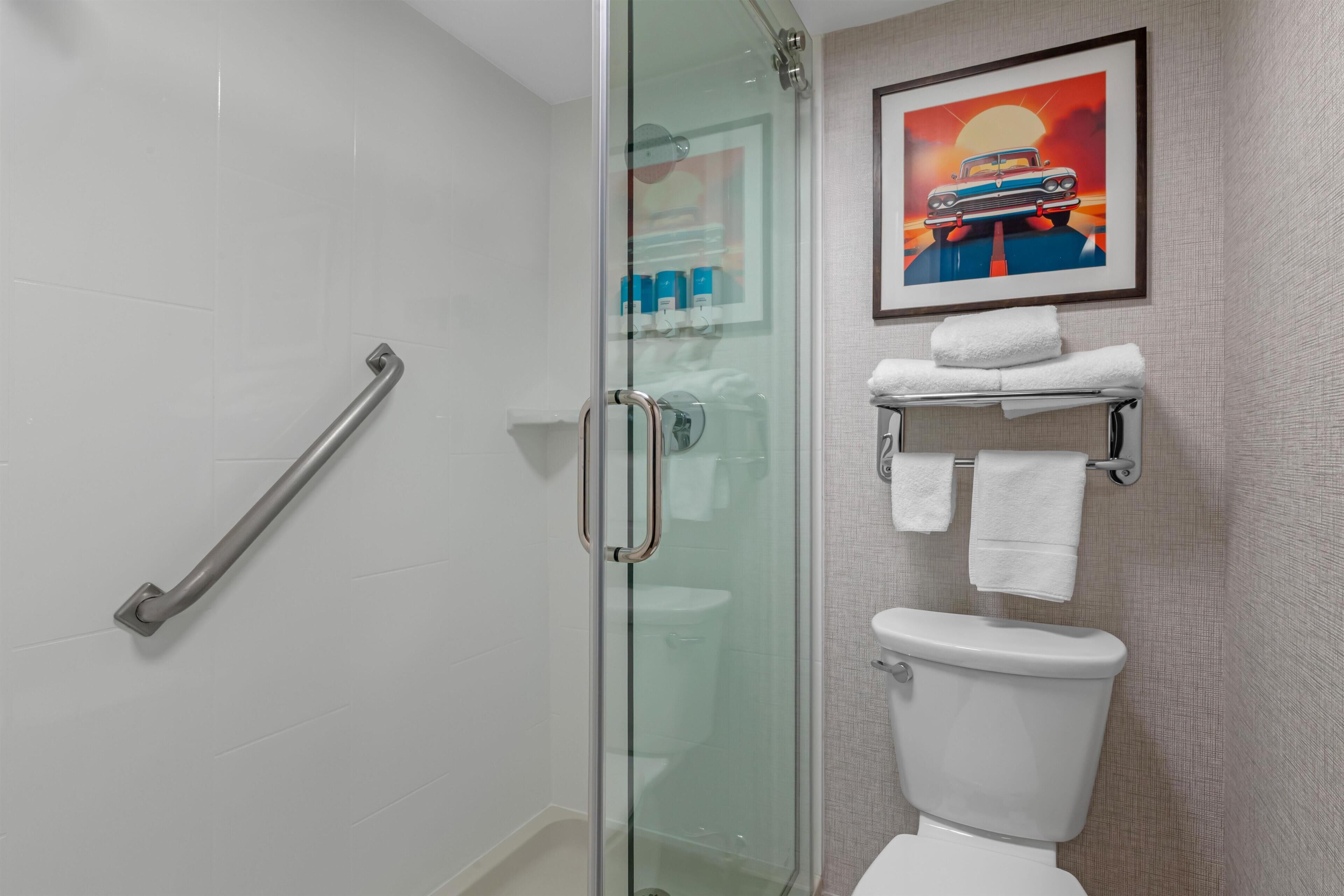 A bathroom with a glass shower enclosure, a white toilet, and a towel rack with multiple towels.