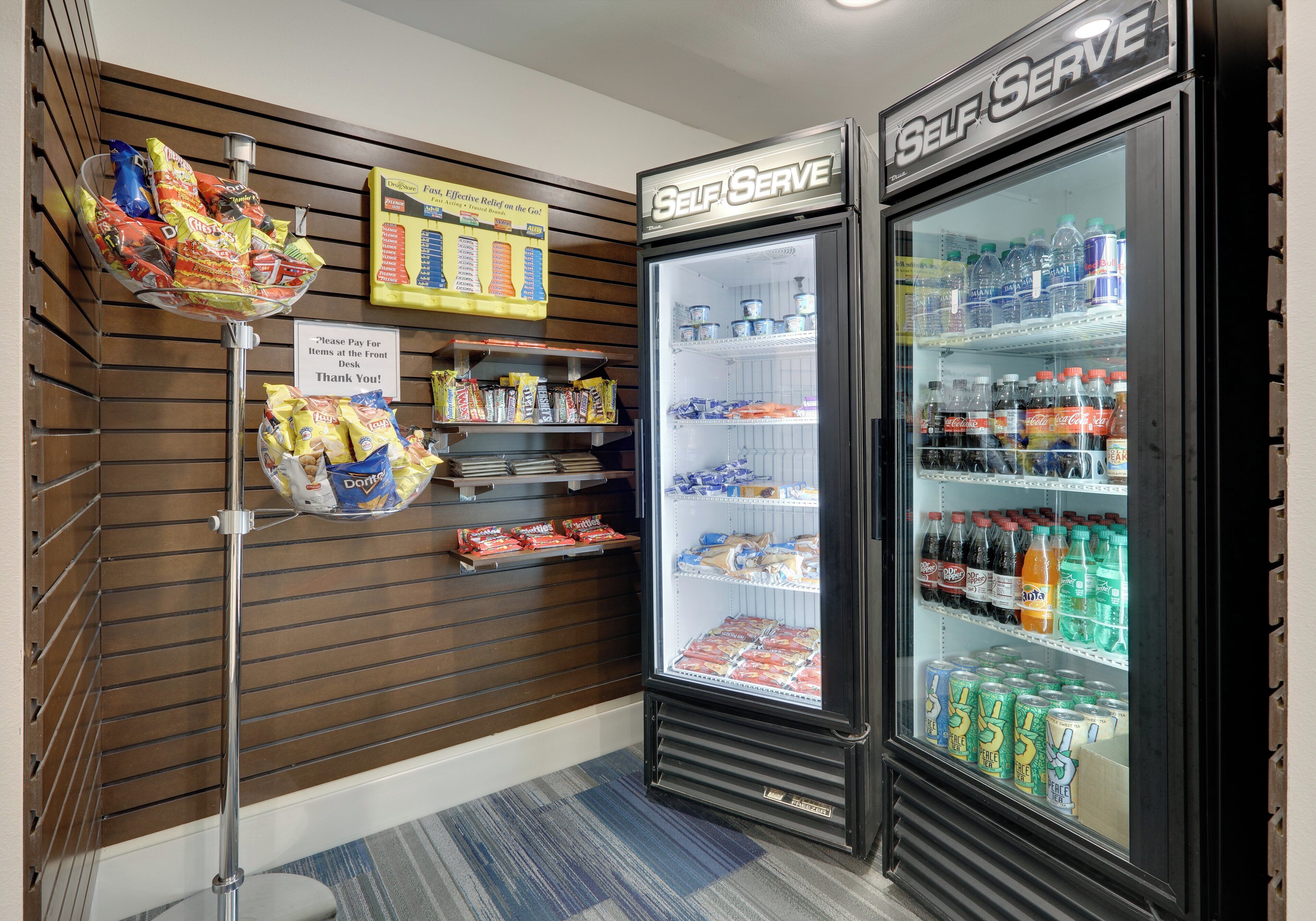 A self-serve beverage refrigerator stocked with various drinks and a snack display with chips and candy.