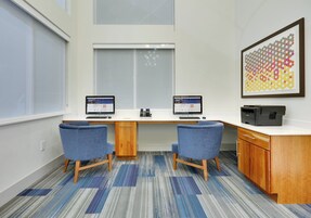 Un espacio de oficina moderno con dos escritorios, sillas, una impresora y un cuadro abstracto grande en la pared.