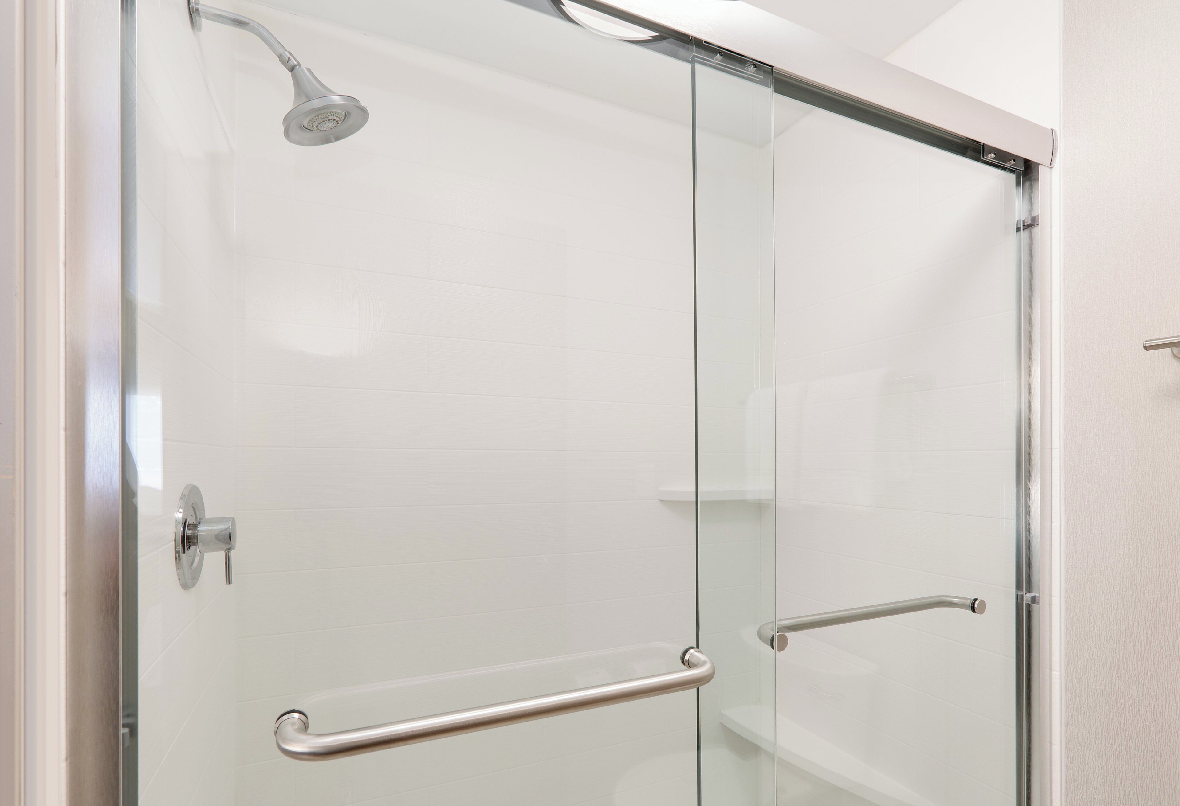 A glass-enclosed shower with a handheld showerhead and two metal grab bars.