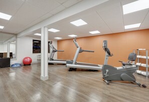 Un gimnasio con equipamiento de ejercicio, piso de madera y un equipo de aire acondicionado instalado en la pared.