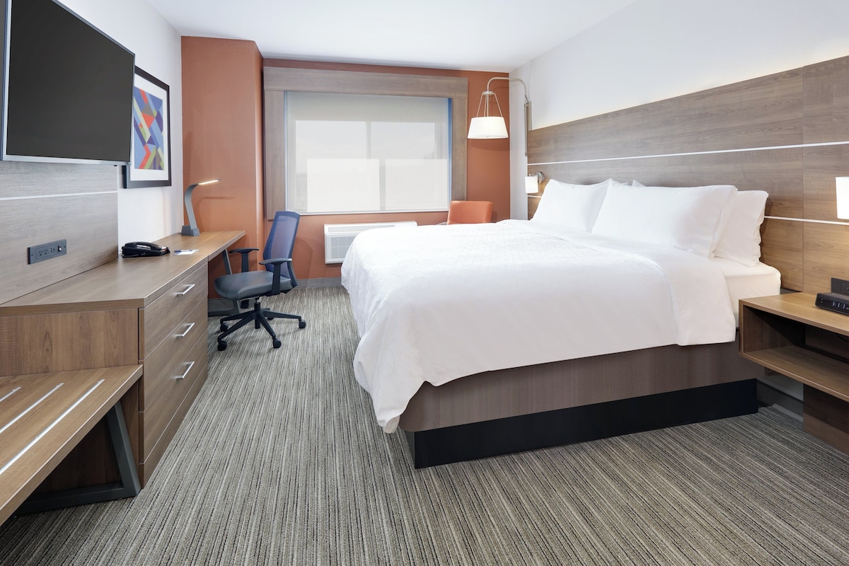 A hotel room with a bed, desk, chair, and a television on the wall.
