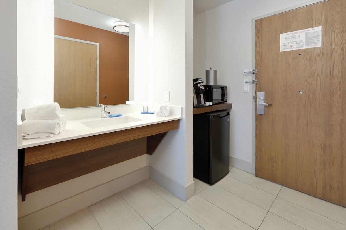 A modern bathroom with a sink, mirror, and a microwave on a shelf.