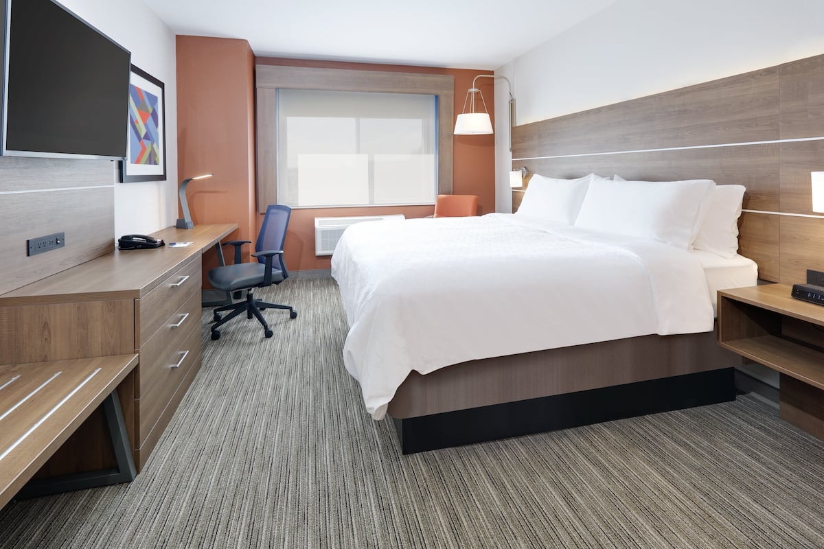 A hotel room with a bed, desk, chair, and a TV.