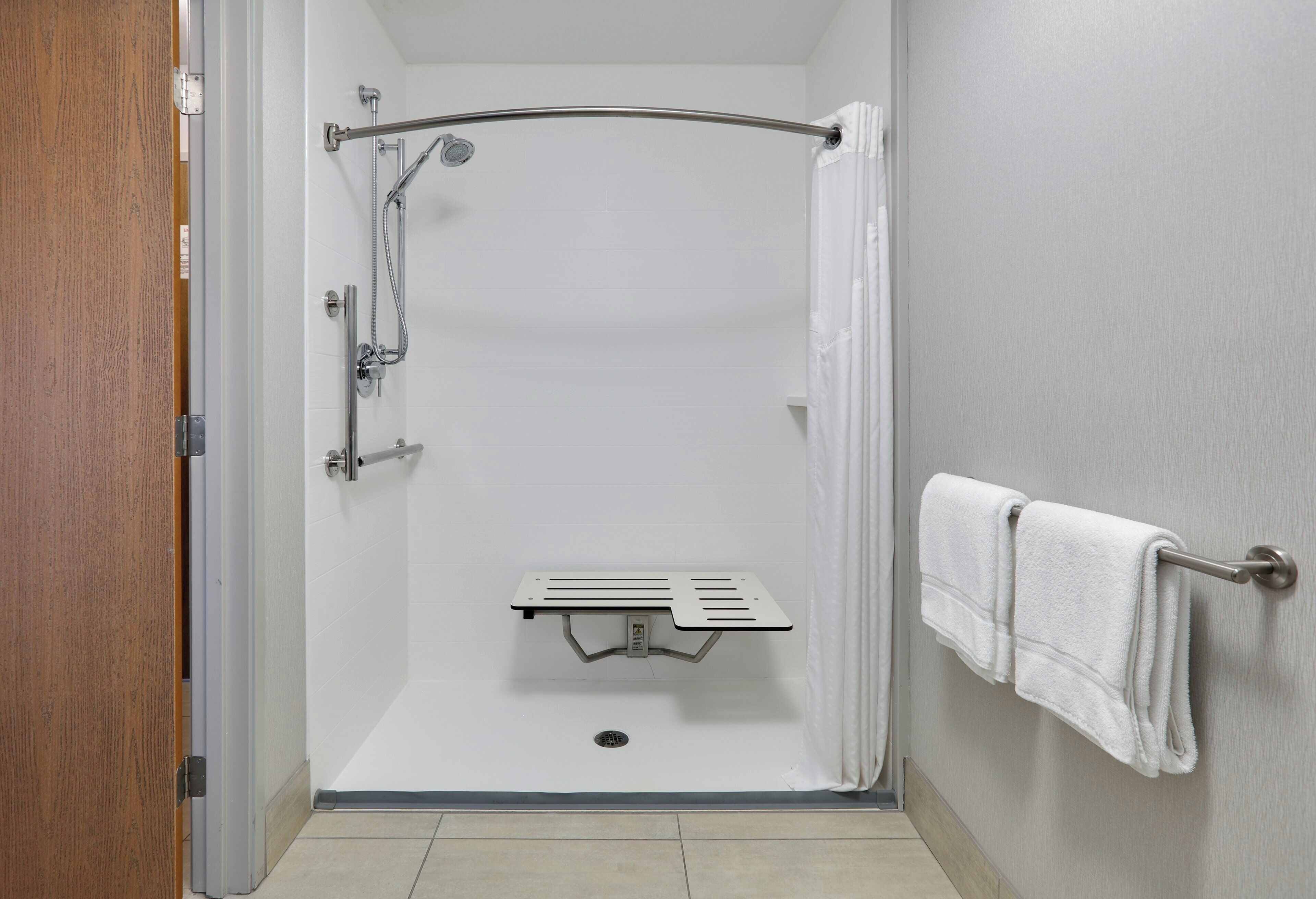 A shower with a handheld showerhead, a towel rack with towels, and a shower control panel.
