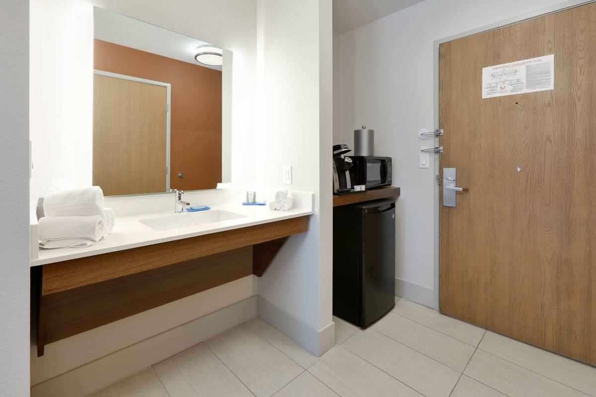 A modern bathroom with a sink, mirror, and a microwave on a shelf.