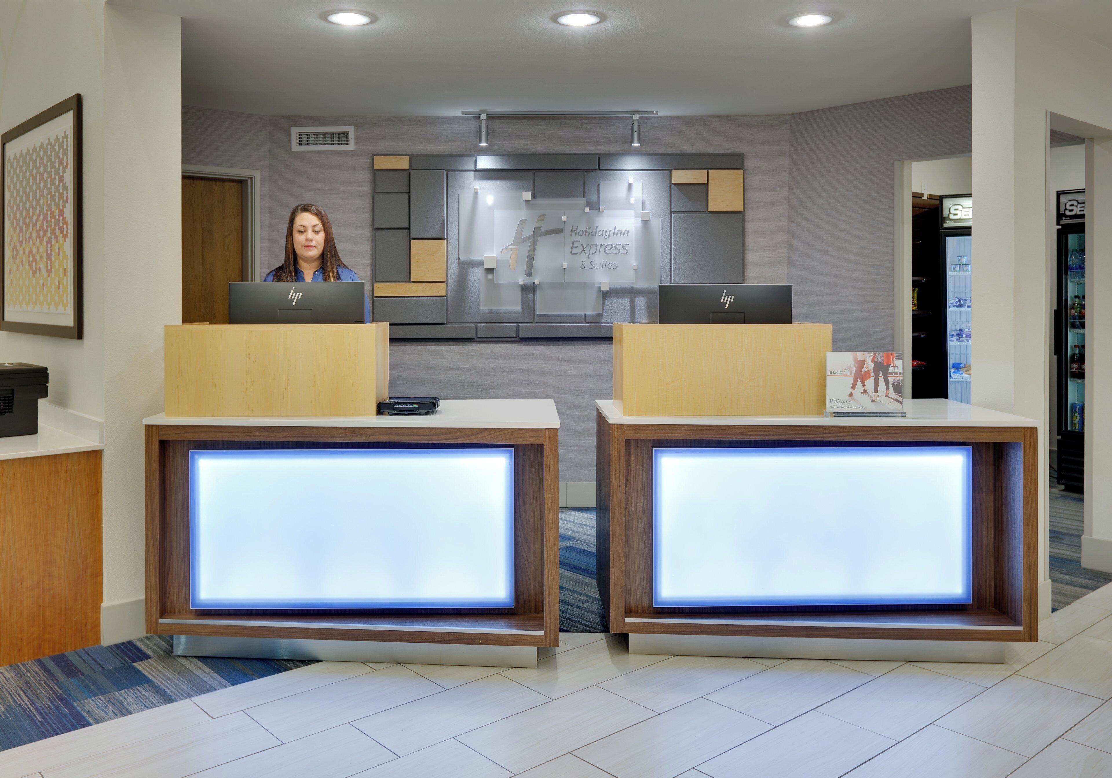 Een receptiebalie met twee computerwerkplekken, een bord met de tekst Holiday Inn Express Suites, en een automaat.