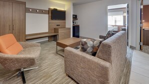 A modern living room with a sofa, armchair, coffee table, and a flat-screen TV mounted on the wall.