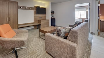 A modern living room with a sofa, armchair, coffee table, and a flat-screen TV mounted on the wall.