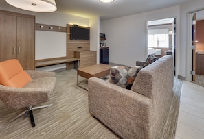 A modern living room with a sofa, armchair, coffee table, and a flat-screen TV mounted on the wall.
