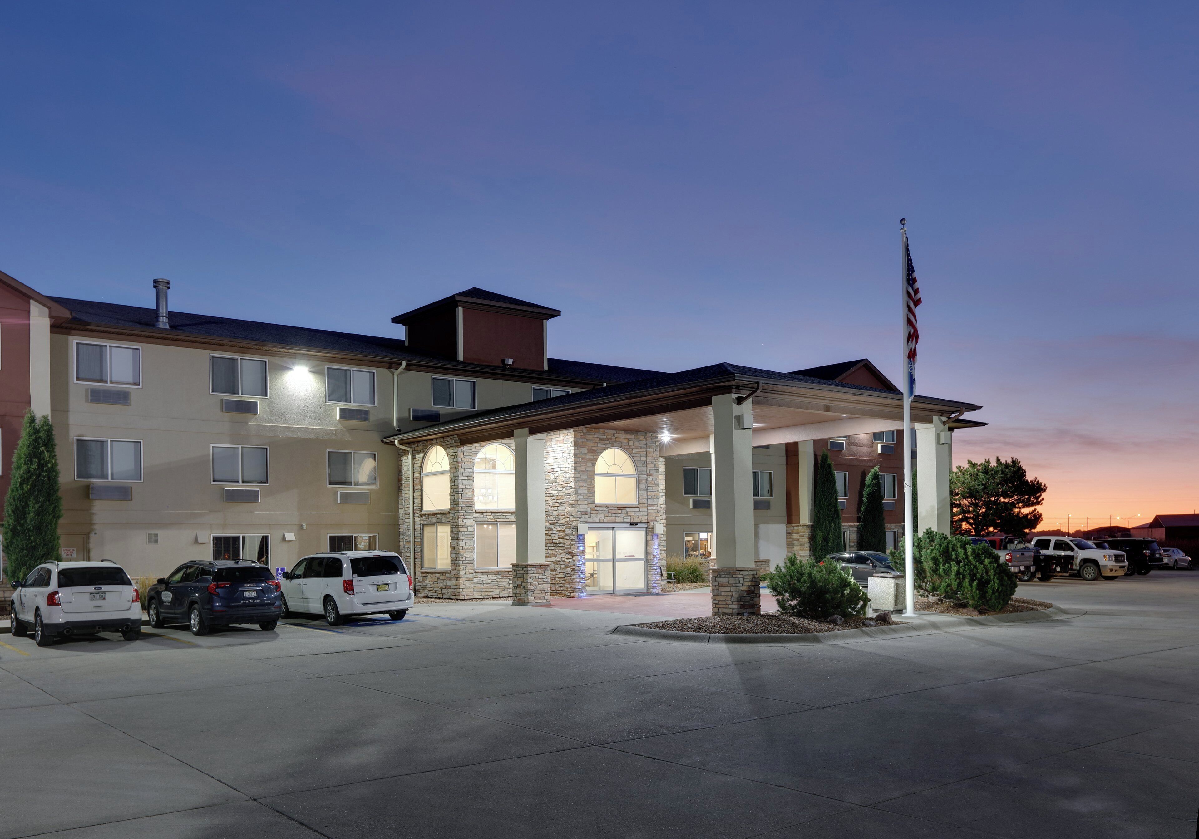 A multi-story hotel with a central courtyard, parking area, and an American flag.