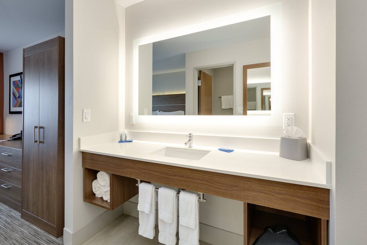 A modern bathroom with a large mirror, two sinks, and a wooden vanity.