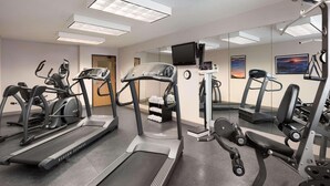 Un gimnasio con cintas de correr, máquinas de pesas y un muro de espejos.