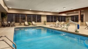 Una piscina interior con sillas de descanso y una mesa, rodeada de ventanas.