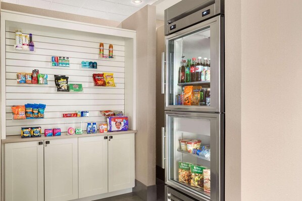 A kitchenette with a refrigerator, freezer, and a shelf stocked with snacks and beverages.
