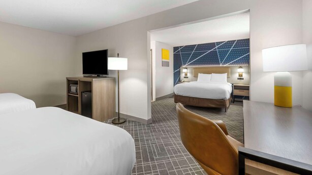 A hotel room with two beds, a desk with a lamp, a TV, and a wall with geometric patterns.