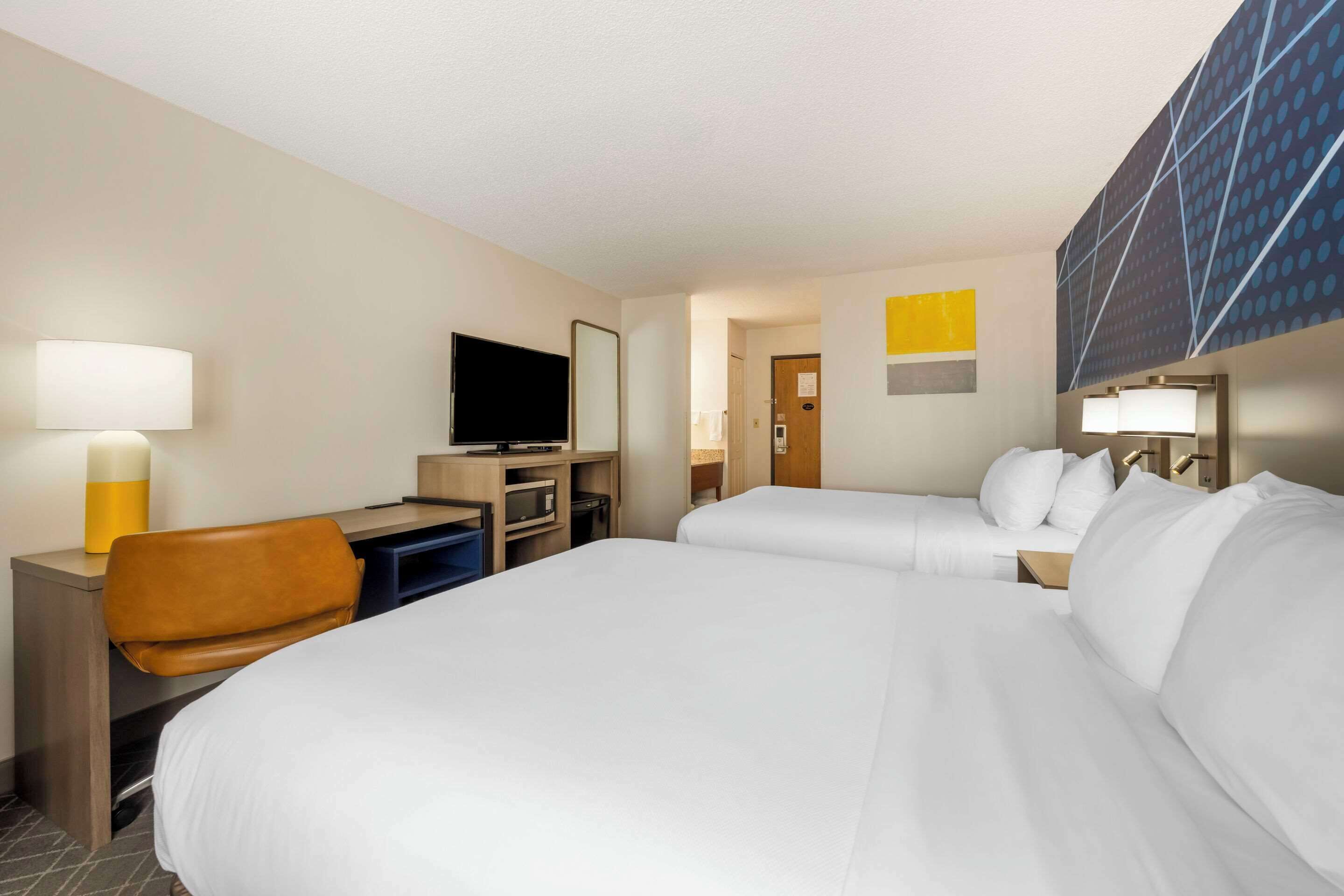 Habitación de hotel con dos camas, un escritorio, un televisor, una silla y un televisor montado en la pared.