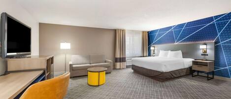 A hotel room with a bed, a desk with a TV, a sofa, a small round table, and a wall with a geometric pattern.