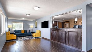 A spacious living area with a sofa, two armchairs, a flat-screen TV, a kitchen counter with a refrigerator, and a large window.