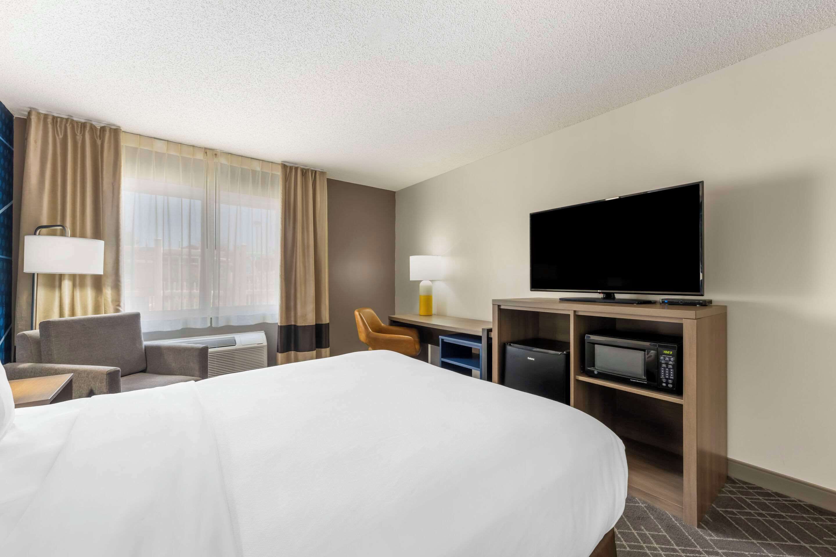 Habitación de hotel con una cama grande, un escritorio con computadora, televisión y microondas.