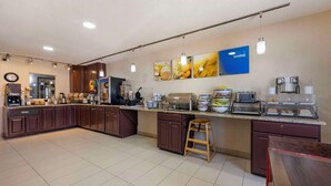 A modern kitchen with dark wood cabinets, a granite countertop, and various appliances including a coffee maker, toaster, and microwave. There are hanging pendant lights and a clock on the wall.