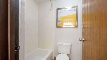 Une salle de bain avec une baignoire blanche, des toilettes blanches et un tableau encadré au mur.