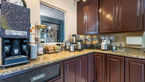 A kitchen with dark brown cabinets, a coffee machine, a clock, and a waste bin.