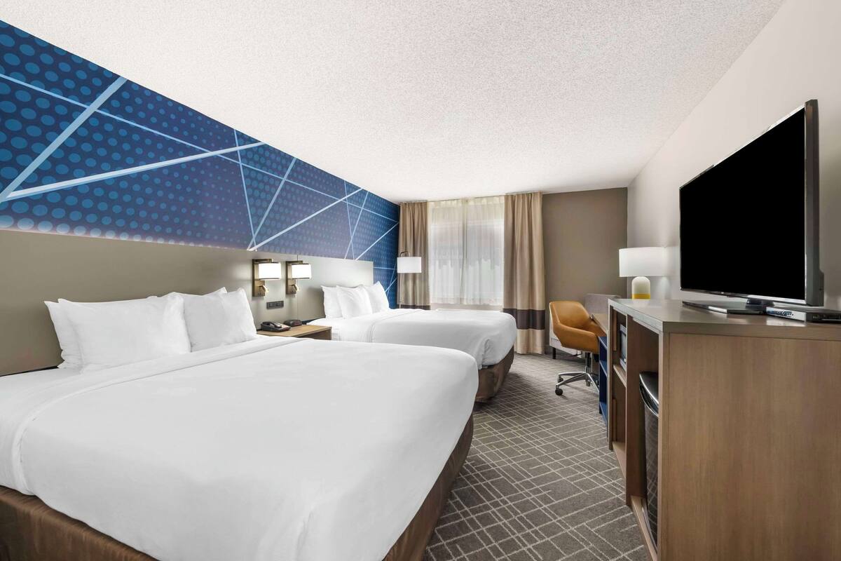 A hotel room with two beds, a desk, a television, and a modern wall design.