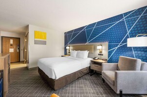 Una habitación de hotel con una cama grande, un escritorio, una silla y una pared con diseño geométrico.