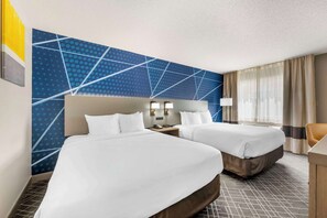 A hotel room with two beds, a nightstand, a lamp, and a window with curtains.