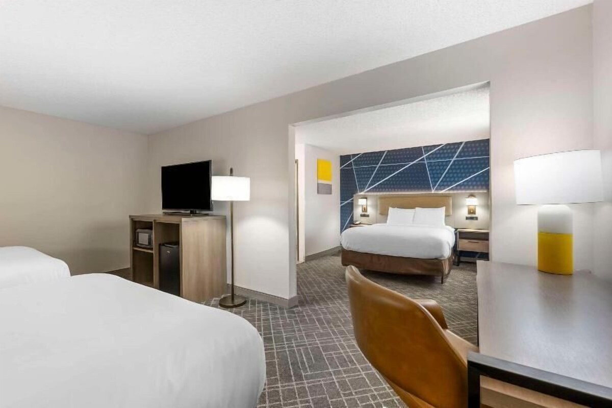 A hotel room with two beds, a TV, a desk, and a lamp.