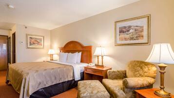 A hotel room with a bed, two bedside lamps, a chair, a nightstand, and two framed pictures on the wall.