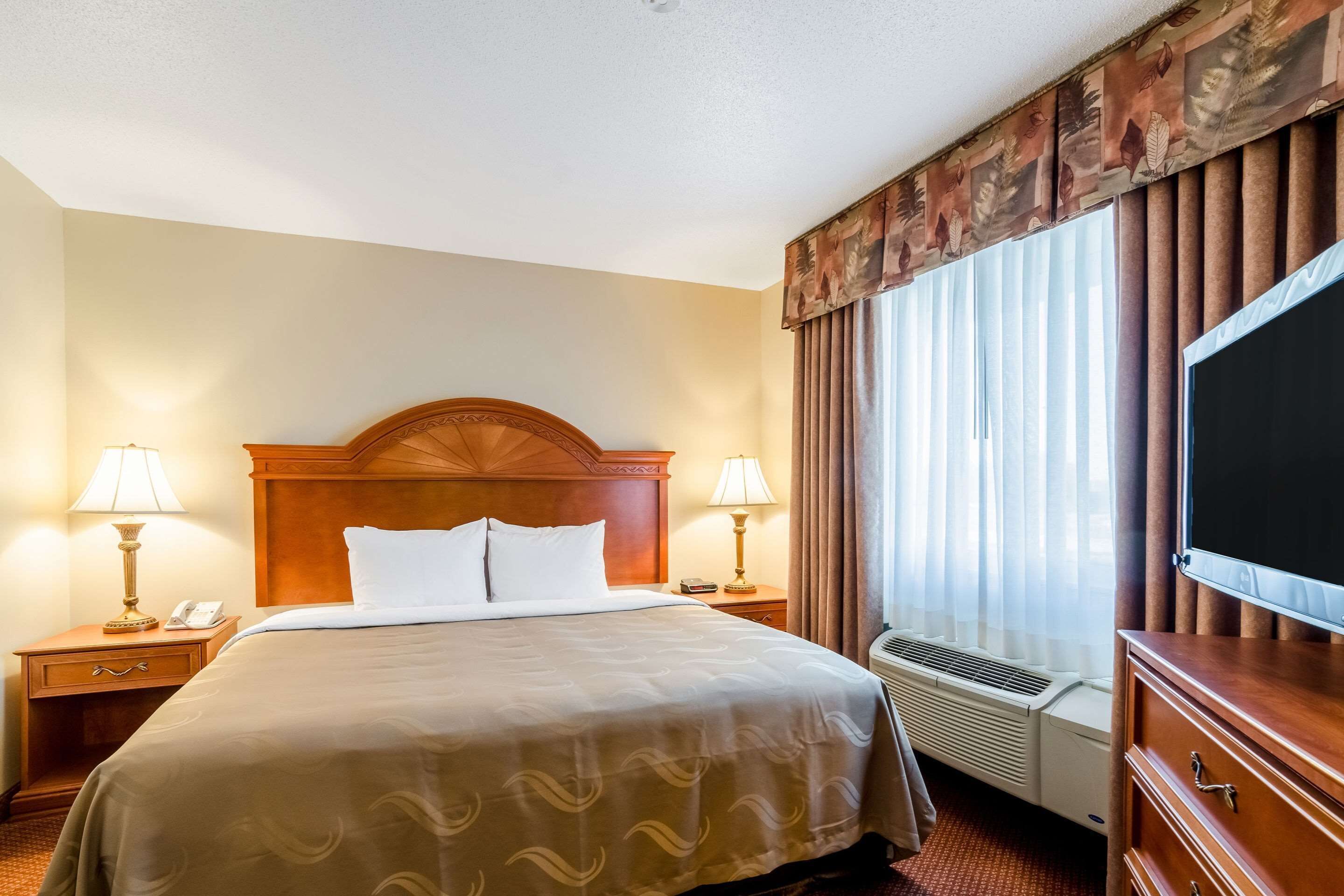 Une chambre d’hôtel avec un grand lit, deux tables de chevet avec des lampes, un téléviseur à écran plat et une fenêtre avec des rideaux.