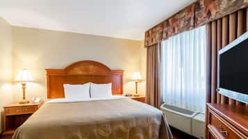 Une chambre d’hôtel avec un grand lit, deux tables de chevet avec des lampes, un téléviseur à écran plat et une fenêtre avec des rideaux.
