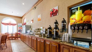Un área de desayuno de hotel con armarios de madera, una estación de café y un dispensador de zumo de frutas.