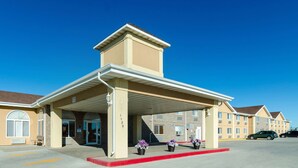 A hotel entrance with a covered area, a parking lot, and a row of hotel buildings in the background.