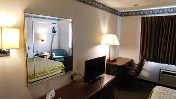 A hotel room with a bed, a desk with a computer, a chair, a mirror, and a lamp.