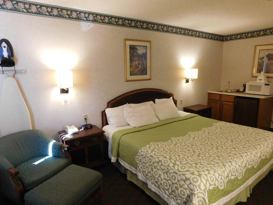 Una habitación de hotel con cama, una silla, una mesita de noche, una lámpara, microondas y refrigerador.